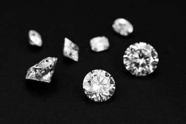 Siyah arka planda bir elmas ve diğer elmasların yakın çekimi. Elmasların hepsi farklı şekil ve boyutlarda ama hepsinin rengi aynı. Lüks ve zarafet kavramı