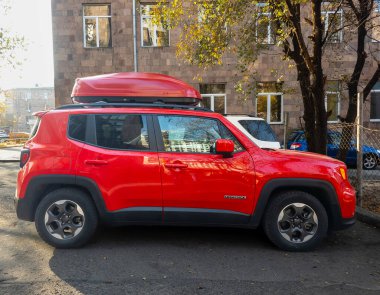 Kırmızı bir Jeep bir binanın önünde park edilmiş. Arabanın tavanında çatı rafı var.