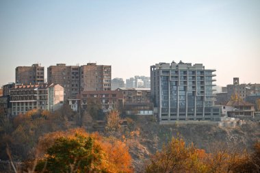 Ortasında büyük bir bina olan bir şehir silueti. Gökyüzü açık ve güneş parlıyor.
