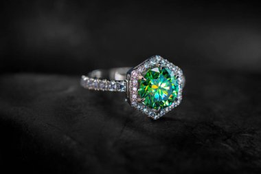 Ortasında elmas olan yeşil ve beyaz bir yüzük. Yüzük siyah bir yüzeyde.