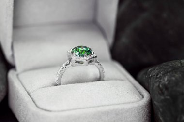 Yeşil ve beyaz bir yüzük beyaz bir kutunun içinde. Yüzük altından yapılmış ve ortasında bir elmas var.