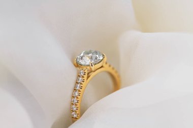 Beyaz bir kumaş üzerinde altın ve elmas bir yüzük sergileniyor. Yüzük aşkın ve bağlılığın sembolüdür.