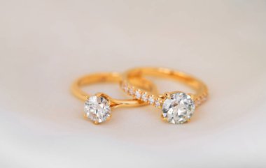 Ortasında elmas olan iki altın ve beyaz yüzük. Halkalar beyaz bir yüzeye yerleştiriliyor.