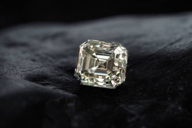 Siyah kadife bir yüzey üzerinde büyük bir elmas duruyor. Elmas kare şeklindedir ve siyah bir arka planla çevrilidir. Görüntünün odak noktası elmas gibi görünüyor.