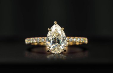 Armut şekilli altın ve beyaz elmas bir yüzük. Yüzük altın bir bantta ve siyah bir yüzey üzerinde duruyor.