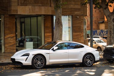 Beyaz bir Porsche Taycan arabası bir binanın önünde park halinde. Araba bir Tesla Model S.