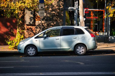 Yolun kenarına gümüş renkli bir Mitsubishi arabası park edilmiş. Araba, üzerinde kırmızı işaret olan bir binanın önünde park halinde.