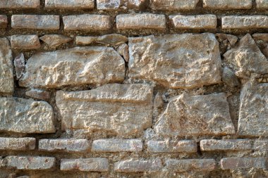 Kaba bir dokusu olan taştan yapılmış bir duvar. Duvar tuğladan yapılmıştır ve gri bir rengi vardır.