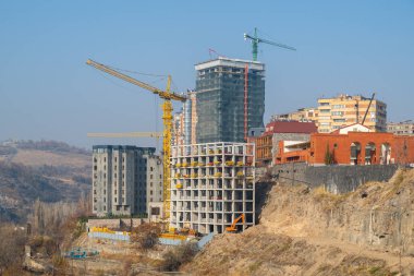 Arkasında büyük bir bina olan bir inşaat alanı. Gökyüzü açık ve güneş parlıyor.