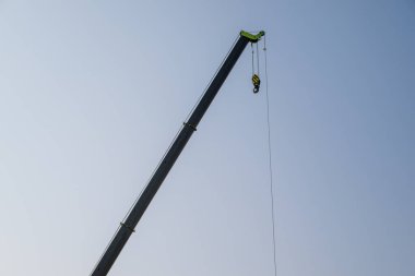 Bir vinç bir insanı havaya kaldırıyor. Vinç uzundur ve uzun bir kolu vardır. Gökyüzü açık ve mavi