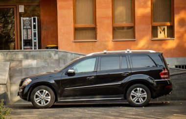 Binanın önüne park etmiş siyah bir Mercedes. Araba yolun kenarına park edilmiş ve yakınlarda bir parkmetre var.