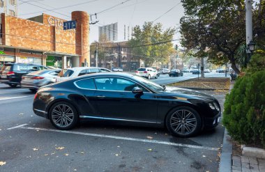 Erivan Ermenistan 11.25.2025. Siyah bir araba bir ağacın yanındaki otoparkta park edilmiş. Araba bir Bentley ve park yerinde duruyor.