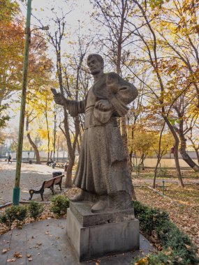 Erivan Ermenistan 11.25.2025. Elinde kitap tutan bir adamın heykeli. Heykel ağaçlar ve banklarla çevrili.