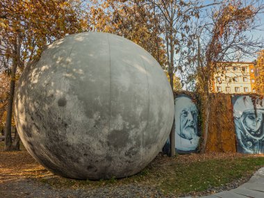 Erivan Ermenistan 11.25.2025. Üzerinde beyaz nokta olan büyük gri bir top bir parkta. Topun arkasındaki duvarda iki insan resmi var.
