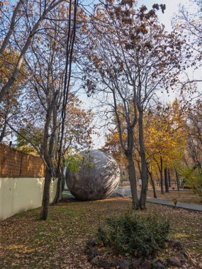 Erivan Ermenistan 11.25.2025. Ağaçlarla çevrili bir parkta büyük bir kaya parçası duruyor. Sahne huzurlu ve sakin, ağaçların yaprakları renk değiştirip yere düşüyor. Kaya görüntünün odak noktasıdır.