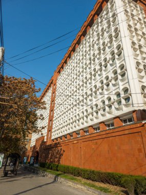 Geniş pencereli ve beyaz yüzlü, Ermenistan Ulusal Politeknik Üniversitesi 'nin yüksek binası. Bina ağaçlar ve çalılarla çevrili.