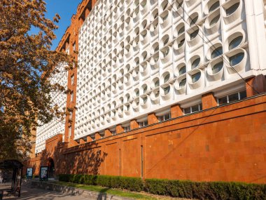 Ermenistan Ulusal Politeknik Üniversitesi 'nin beyaz yüzlü ve kırmızı çizgili büyük bir binası. Bina ağaçlarla çevrili ve bir sürü penceresi var.