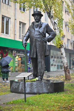 Bir Alexander Mantashev heykeli şapka takıyor ve şemsiye tutuyor. Heykel bir şehir parkında.