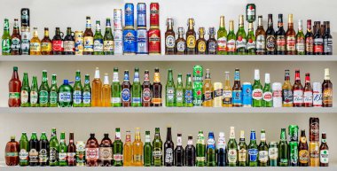 Çeşitli marka ve renklerde bira şişeleriyle dolu bir raf. Tüketim için çeşitli bira türlerine sahip bolluk ve çeşitlilik kavramı