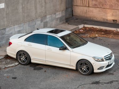 Erivan Ermenistan 12.5.2025. Yolun kenarına park etmiş beyaz bir Mercedes. Araba tuğla bir duvarın önünde duruyor.