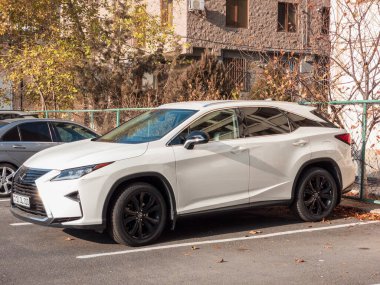 Erivan Ermenistan 12.5.2025. Siyah lastikli beyaz bir araba bir otoparkta park edilmiş. Araba yeşil bir çitin yanında park edilmiş.