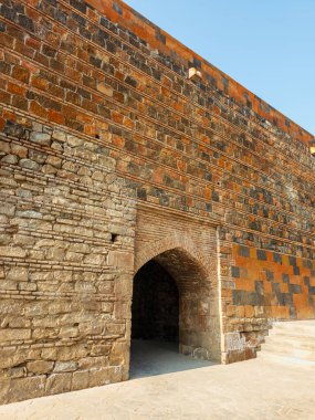 Bir binanın girişi taştan yapılmıştır ve küçük bir kemer yolu vardır. Taş kahverengi ve kemer yolu dar.