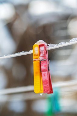 İki kırmızı ve sarı mandal bir hatta asılı. Mandallar karla kaplı.