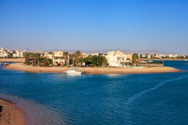 El Gouna Mısır. Suyun ortasında küçük bir adası olan bir sahil. Ada evlerle çevrili ve bir tekne suya yanaştı. Su sakin ve gökyüzü berrak.