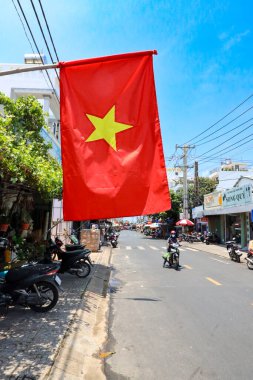 İzlanda Phu Quoc Vietnam 5.7.2025. Sarı yıldızlı kırmızı bir bayrak direkten sarkıyor. Bayrak, kenarda birkaç motosikletin park ettiği bir şehir caddesinde.