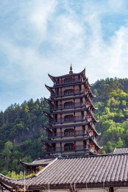 Chongqing Çin 4.7.2025. Yeşil dağlar ve doğa ile çevrili geleneksel Çin pagoda kulesi kıvrımlı kiremitli çatılar ve kırmızı fenerler