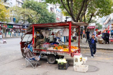 Chongqing Çin 'de bir adam sokakta bir kamyondan meyve satıyor. Bölgede dolaşan birkaç kişi var.