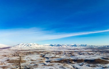 Arka planda bir dağ sırası olan açık mavi bir gökyüzü. Gökyüzü çok parlak ve dağlar karla kaplı.