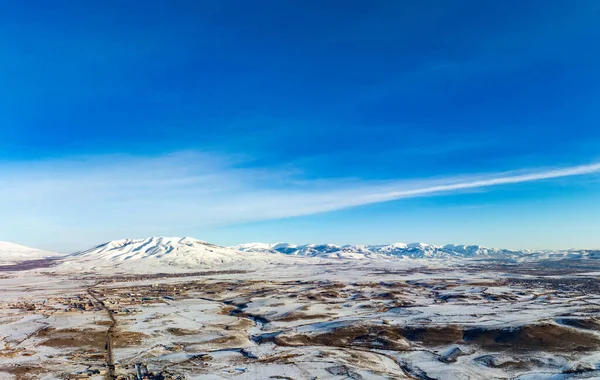 Arka planda bir dağ sırası olan açık mavi bir gökyüzü. Gökyüzü çok parlak ve dağlar karla kaplı.