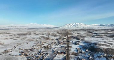 Uzakta küçük bir kasabası olan karlı bir manzara. Gökyüzü açık ve mavidir, ve güneş parlıyor. Sahne huzurlu ve huzurlu bir atmosfer veriyor.