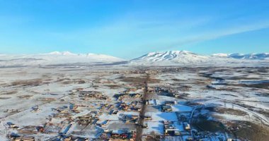 Uzakta küçük bir kasabası olan karlı bir manzara. Gökyüzü açık ve mavidir, ve güneş parlıyor. Sahne huzurlu ve huzurlu bir atmosfer veriyor.