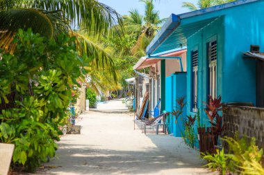 Parlak mavi kulübeler sakin bir tropikal yol çiziyor. Bereketli yeşil palmiyeler ılık rüzgarda sallanıyor. Güneş ışığı kumlu yolda yavaşça yürür. Sandalyeler renkli duvarların yanında rahatlamaya davet ediyor
