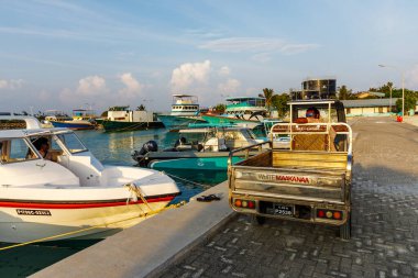 Tekneleri ve kırsal bir kamyonu olan güneşli bir liman. Sakin suların ve yumuşak dalgaların üzerindeki berrak gökyüzü. Canlı renkler tropikal ortamı yansıtır. İnsanlar rahatlıyor ya da geziniyor, deniz kenarında eğleniyorlar.