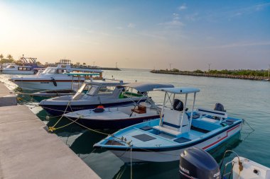 Güneşli tekneler sakin liman rıhtımlarında dinleniyor. Mavi ve beyaz gemiler yavaşça beton iskelelerin yanında yüzerler. Yumuşak altın ışık suyun yüzeyini boyar. Huzurlu deniz manzarasını kimse bozamaz.