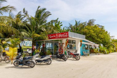 Hindistan cevizi ağaçları yol kenarındaki renkli tezgahın yanında sallanıyor. Motosikletler neşeli, davetkar bir mağazanın önünde dinlenirler. Yumuşak, altın güneş ışığıyla tropik bir manzara. İnsanlar rahat görünüyor, dinlenmekten zevk alıyorlar.