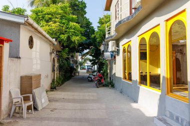 Parlak sarı dükkan önleri olan güneşli bir sokak. Yemyeşil ağaçlar dar yolda. Scooter duvara yaslanıyor ve cazibesini arttırıyor. Beyaz sandalye istiflenmiş sandıkların yanında boş duruyor.