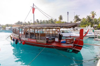 Kırmızı tekne sakin turkuaz sularda yüzer. Ahşap parmaklıkları ve açık oturma alanı olan bir kulübe. Tropikal palmiyeler uzak kıyı şeridi boyunca uzanır. Güneşli bir gün, hafif bir esinti, huzurlu bir atmosfer.