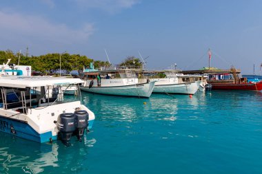 Berrak turkuaz su, huzurlu tekneler beşikte. Beyaz ve kırmızı gemiler sakin limanda dinleniyor. Güneş ışığı hafif dalgalanmalarla parlar. Bereketli yeşil ağaçlar uzak kıyı şeridinde. Serene sahnesi seyahate davet eder
