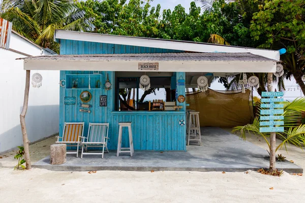 Samimi mavi kulübe kumlu kumsalın yanında. Güneşli tenteler, basit bar oturakları. Tropik ağaçlar sakin sahil manzarasını çerçeveliyor. Canlı turkuaz duvarlar ada cazibesi yayar. Huzurlu insanlar yok.