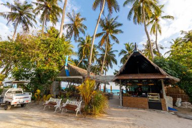 Tropik sahil kenarı barı palmiye ağaçlarının altında. Güneş ışığı, okyanus ufkuyla birleşir. Köy kabininin yakınına park edilmiş paslı bir kamyon. Huzur arayan tatilciler için sakin, davetkar bir ortam. Seyahat ve tatil için mükemmel.