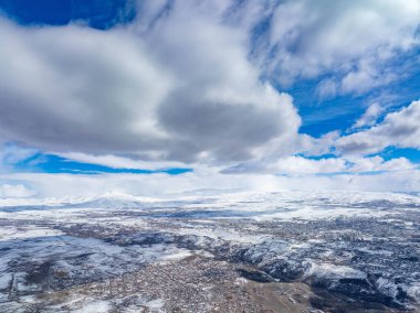 Karla kaplı vadi dramatik bulutların altında. Kasaba dağların arasına kurulmuş. Huzurlu kış manzarası. Seyahat, tatil veya doğa teması için ideal