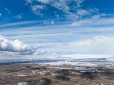 Karla kaplı düzlükler, dağınık bulutlarla dolu parlak mavi gökyüzünün altında uzanıyor. Manzara el değmemiş vahşi doğayı gösteriyor, sessiz ve huzurlu. Seyahat, doğa veya kış temalı projeler için ideal