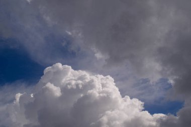 Büyük, tüylü beyaz bulutlar derin mavi gökyüzüne hükmediyor. Koyu gri fırtına bulutları gökyüzünde beliriyor ve dram katıyor. Görüntü, yaklaşan hava değişikliğini ya da fırtına öncesi sessizliği öneriyor. Havayla ilgili içerik için kullanışlı