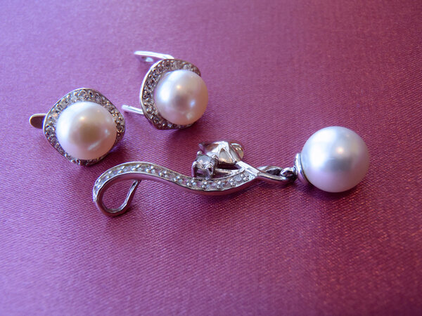Earrings and pendent with sea pearls and cubic zirconias on a pink background close up.