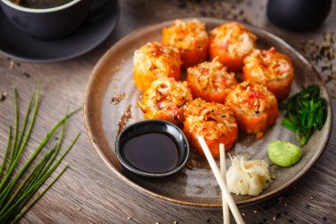 Somon, yengeç, salatalık, avokado, uçan balık yumurtası ve yemek çubuğu, soya sosu, wasabi ve zencefilli baharatlı soslu fırında suşi ruloları. Japon deniz ürünleri restoranda öğle yemeği için servis edilir..