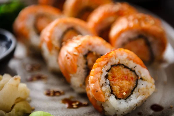 Baked sushi maki rolls with salmon, crab and spicy sauce on a plate with chopsticks, soy sauce, wasabi and ginger. Japanese traditional fish food closeup served for lunch in modern gourmet restaurant — Stock Photo, Image